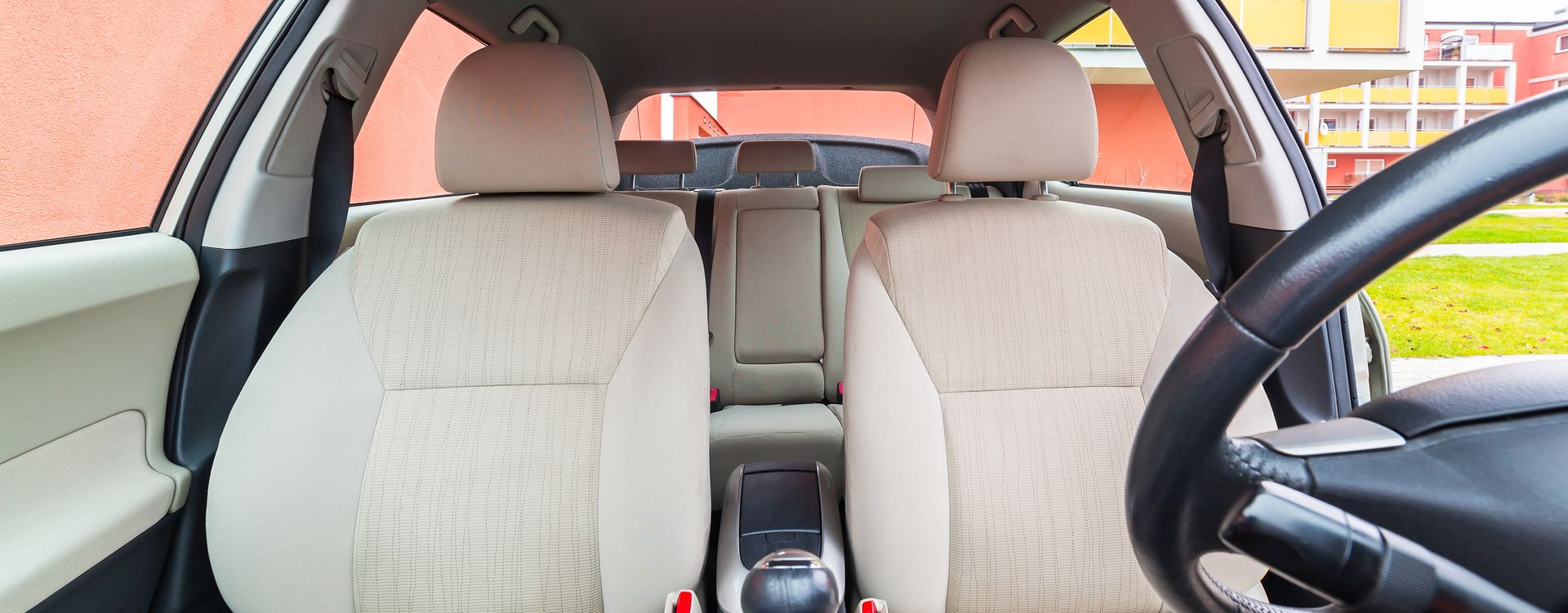 Vue intérieure d'une voiture avec des sièges beiges, un volant et un aperçu d'un bâtiment extérieur.