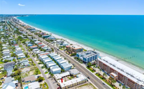 Aerial view of a coastal neighborhood with white buildings beside turquoise ocean and sandy beach