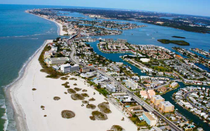 Aerial view of a coastal resort town with white sandy beach, blue ocean, and marina-lined waterways