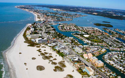 Aerial view of a coastal resort town with white sandy beach, blue ocean, and marina-lined waterways