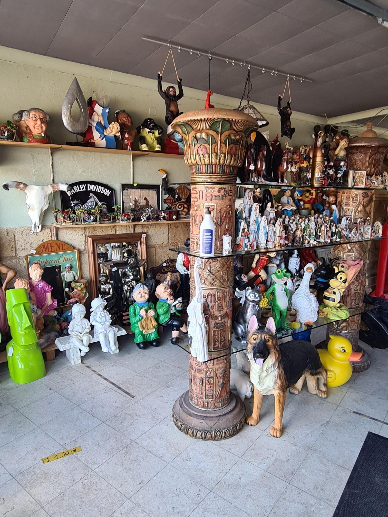 Interieur van een speelgoed- en poppenwinkel met planken vol beeldjes en een gebeeldhouwde pilaar als vitrine in het midden.
