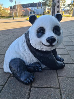 Een klein pandabeeldje staat overdag op een geplaveide stoep.