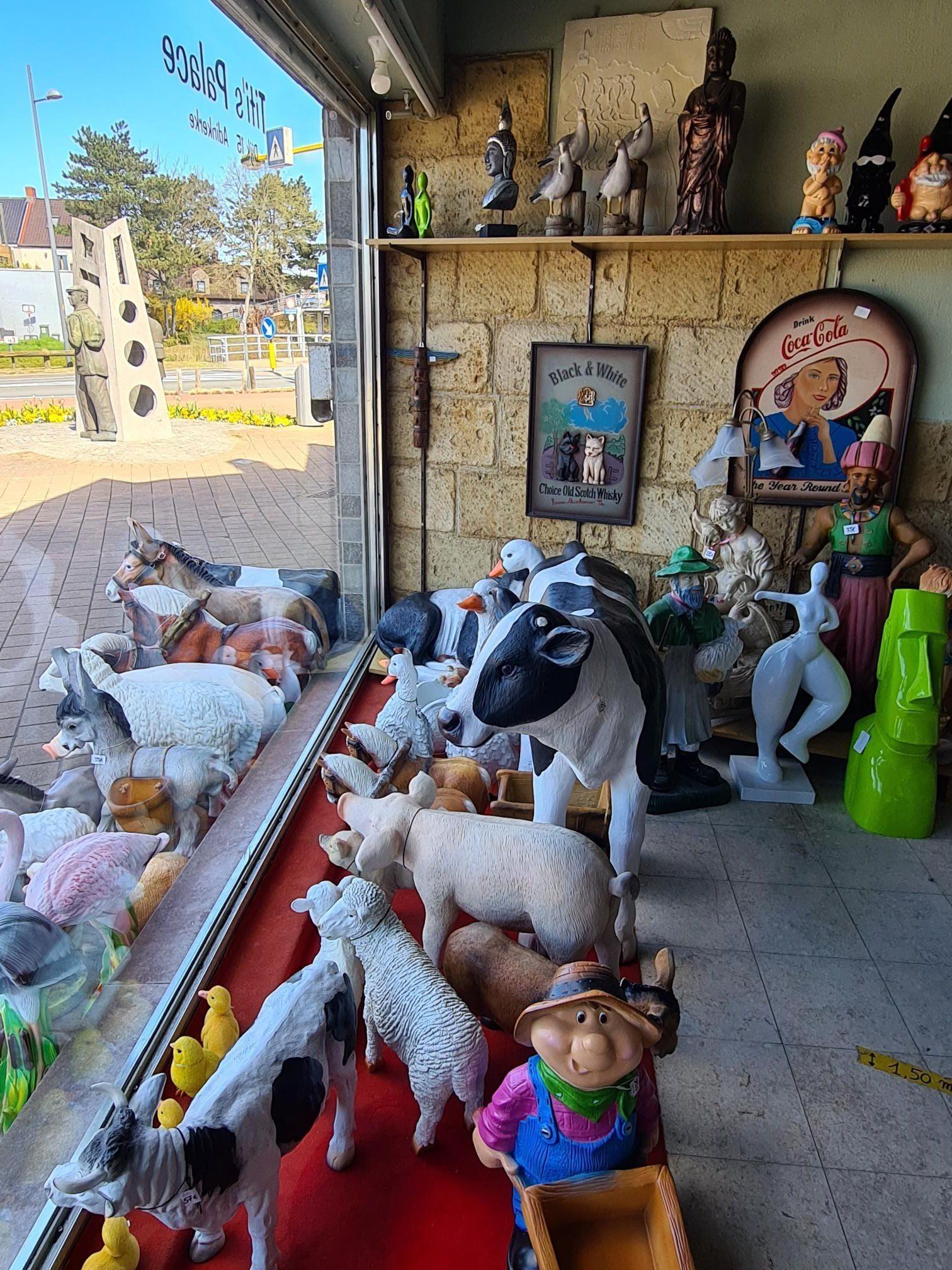 Pluche dieren en poppen tentoongesteld in een etalage naast decoratieve beeldjes en ingelijste kunstwerken.