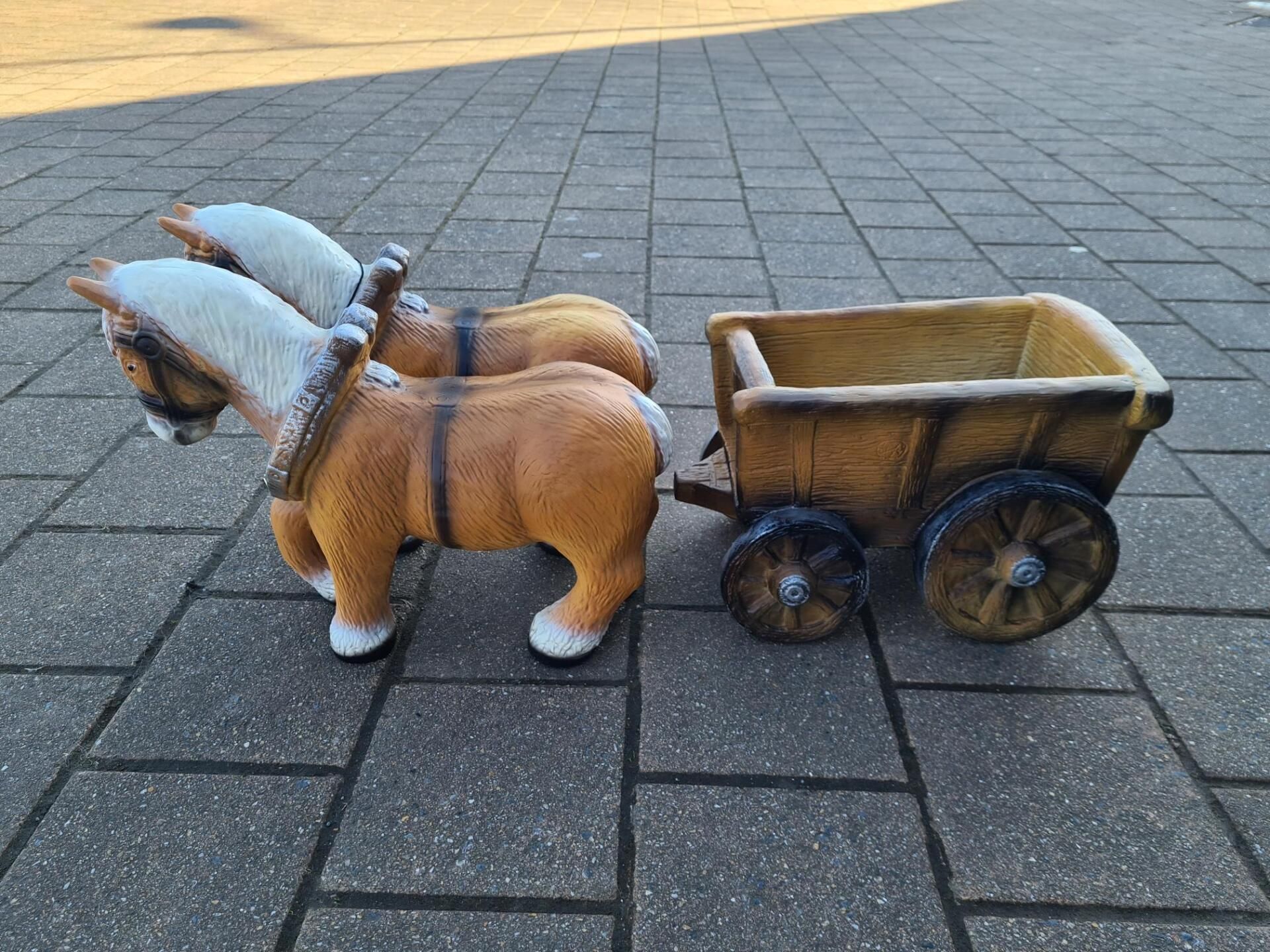 Een klein speelgoedpaardje trekt een houten karretje over een geplaveide ondergrond.