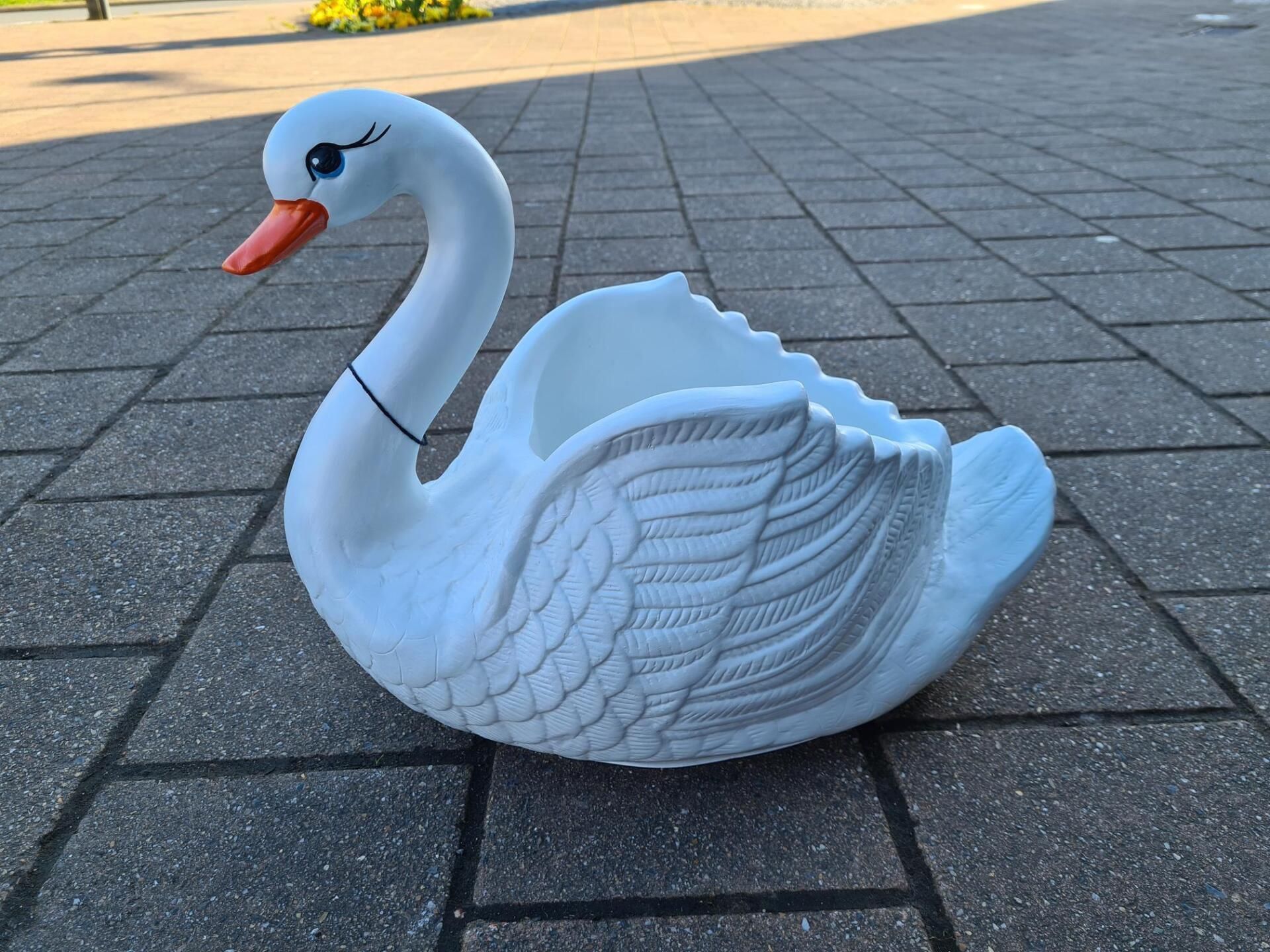 Een wit, zwaanvormig beeld op een geplaveid trottoir in de buitenlucht, met een rode snavel en gebeeldhouwde veerdetails.