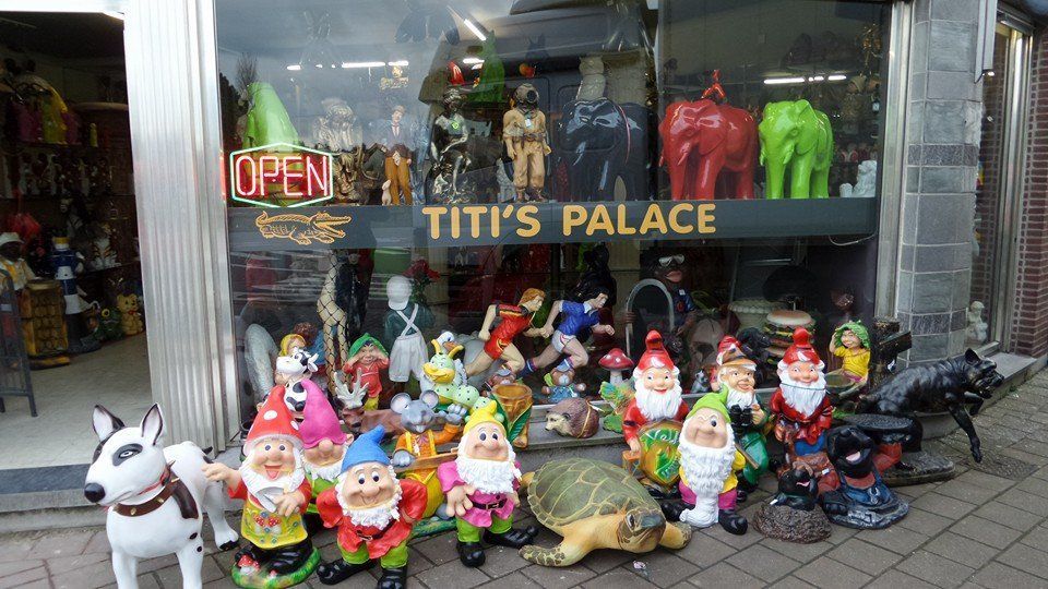 Een etalage met kleurrijke tuinkabouters en dierenbeeldjes voor het paleis van Titi, met een bordje 'OPEN'.