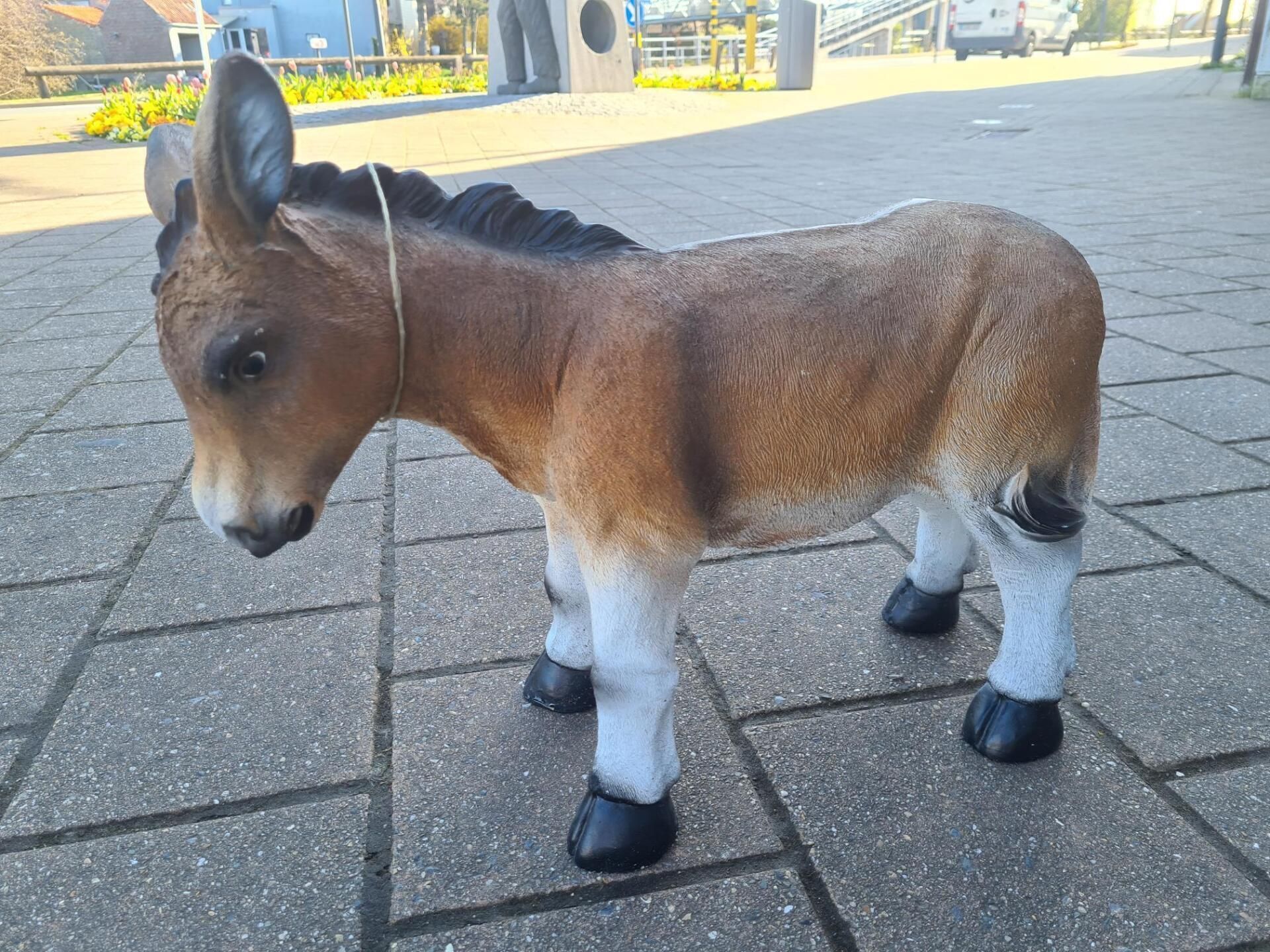 Een klein bruin-wit speelgoedezeltje staat op een geplaveid pad buiten.