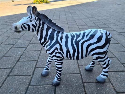 Klein zebrabeeldje op een geplaveid trottoir, in zijaanzicht weergegeven.