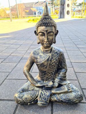 Bronzen Boeddhabeeld, zittend met gekruiste benen, op een betegeld terras in de zon.