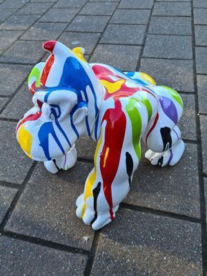 Kleurrijk beschilderd hondenbeeld met abstracte rode, blauwe, gele en groene wervelingen op een geplaveide stoep.