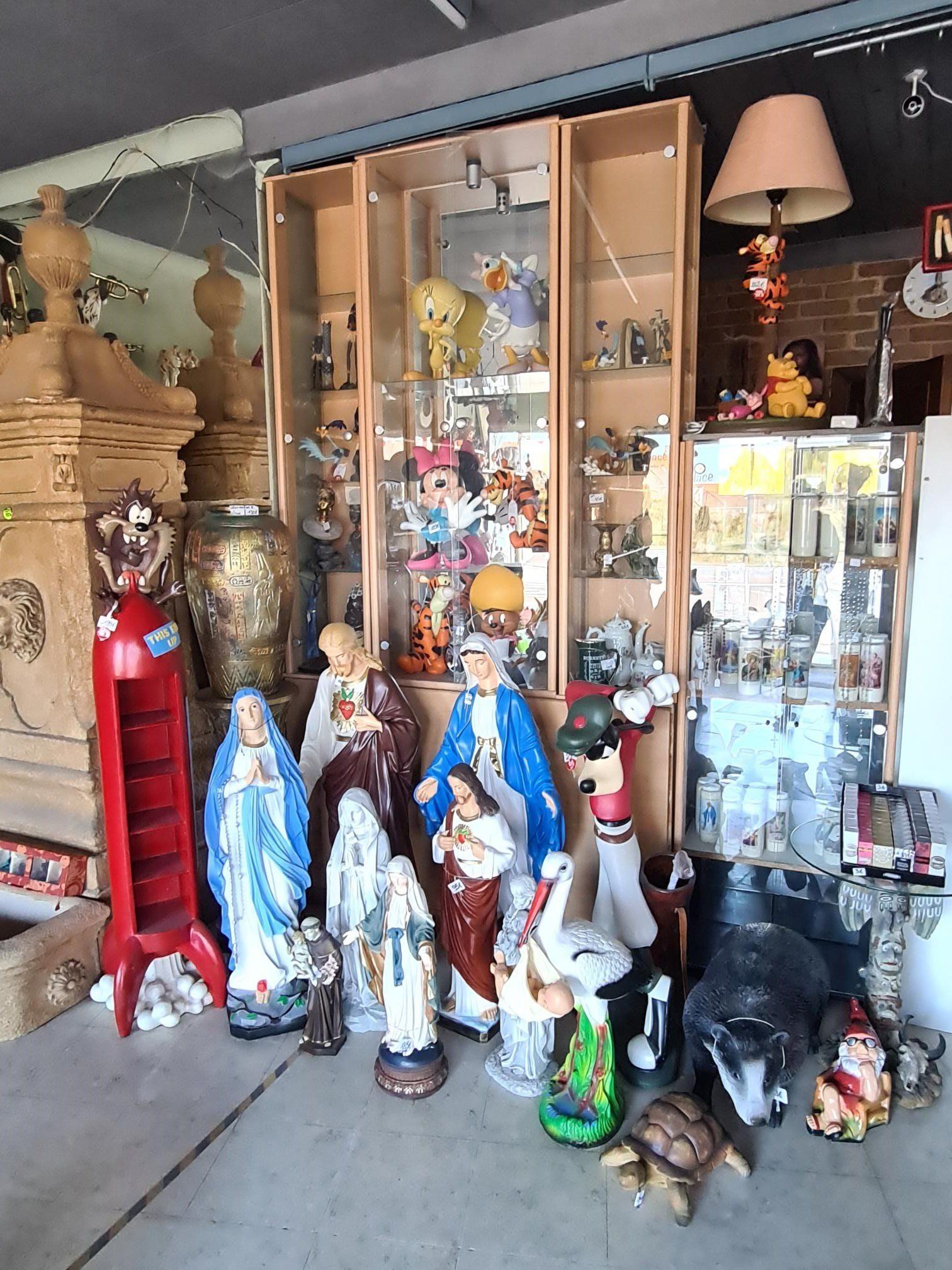 Een winkel toont een assortiment religieuze beelden en beeldjes, waaronder blauwe en rode Mariabeeldjes.