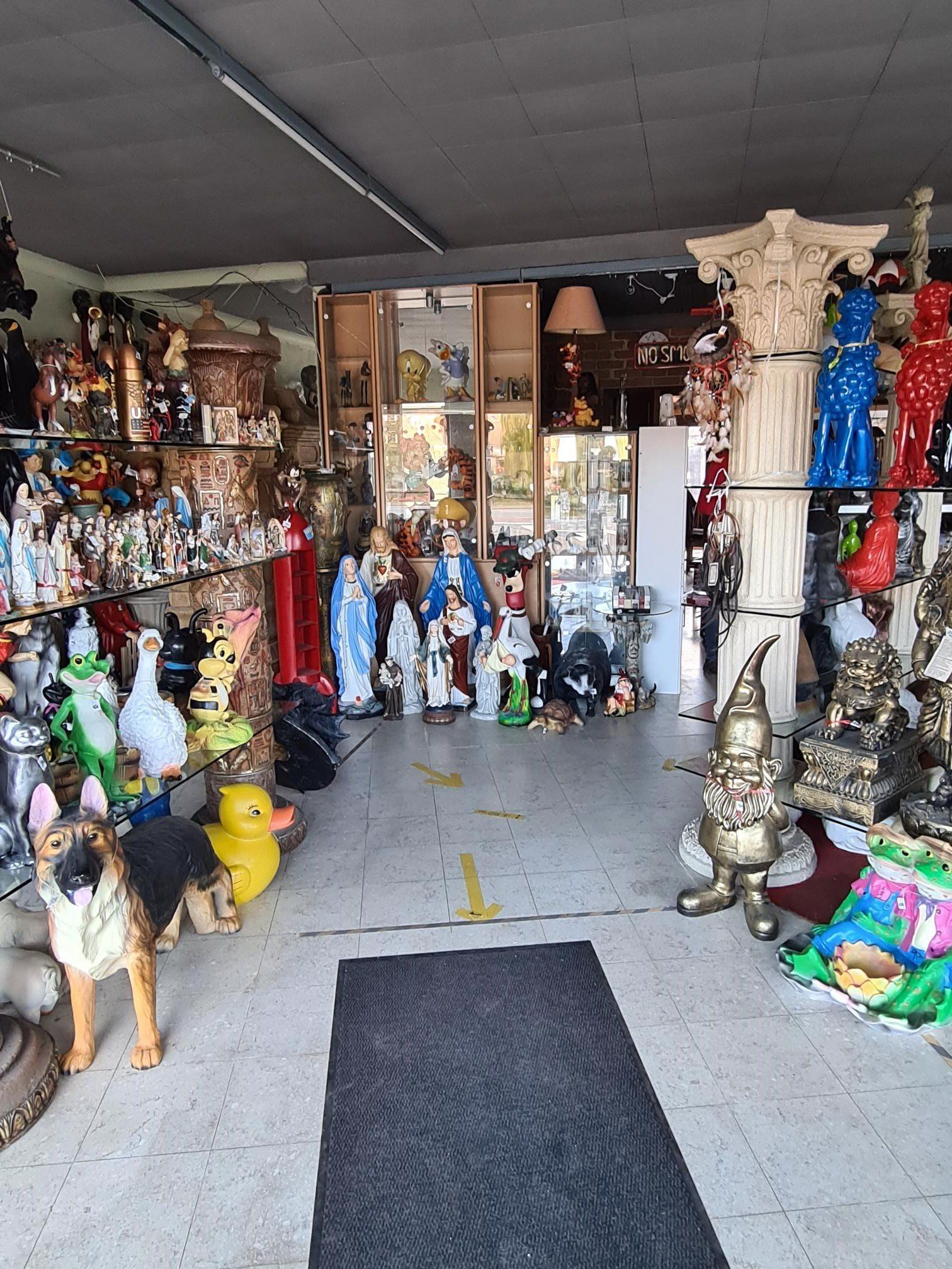 Interieur van een cadeauwinkel met planken vol beeldjes, standbeelden en kleurrijke souvenirs onder een donker plafond.