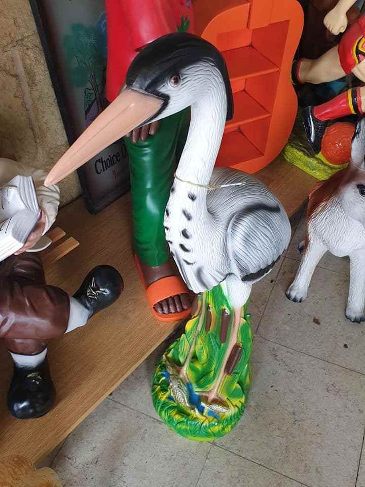 Een wit-zwart ooievaarsbeeldje staat op een kleurrijke sokkel tussen andere speeltjes op een plank.