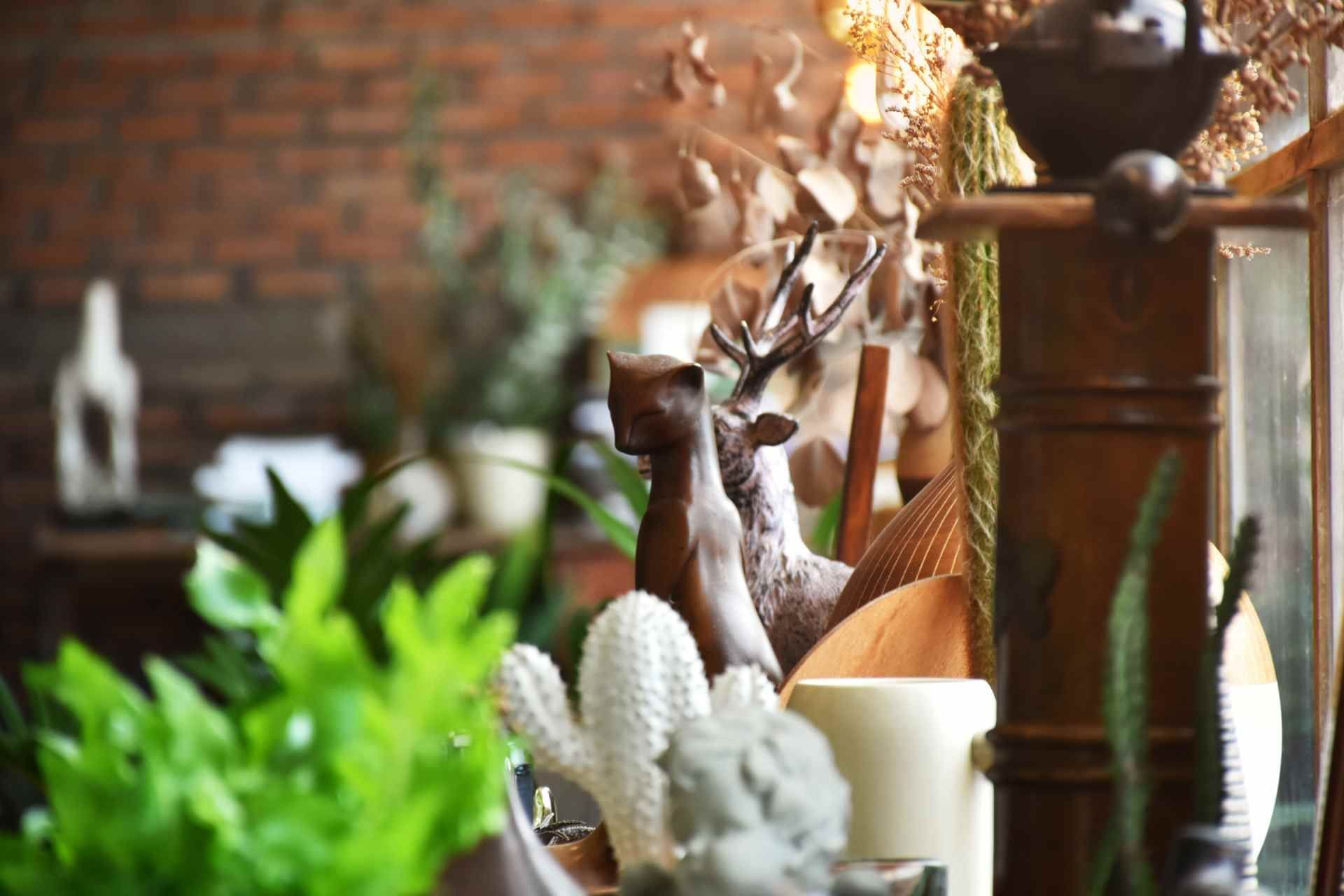 Decoratieve keramische beeldjes en planten op een tafel tegen een bakstenen muur.