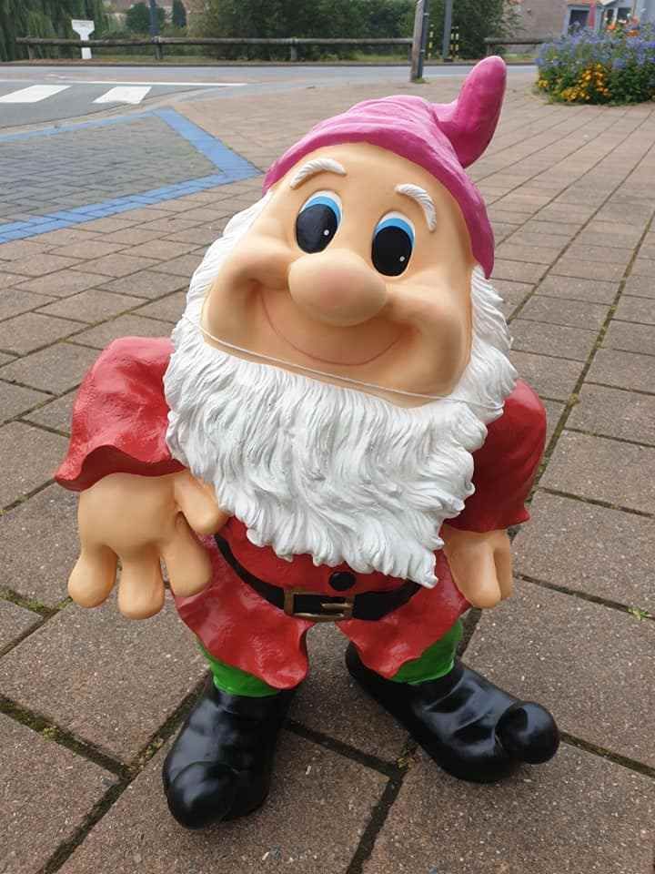 Een klein tuinkabouterbeeldje met een roze hoed, rode kleren en zwarte schoenen op een bestraat pad.