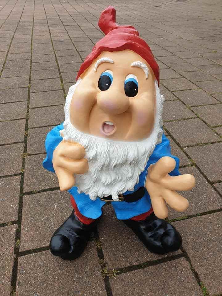 Tuinkabouterfiguur met rode hoed, witte baard, blauwe kleren en zwarte schoenen op een stenen terras.
