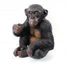 Klein zwart babychimpanseefiguurtje dat zit en één hand omhoog houdt, op een witte achtergrond.