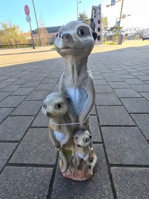 Drie stokstaartjesbeeldjes op een stoep, waarvan er één rechtop staat en twee eronder gluren.