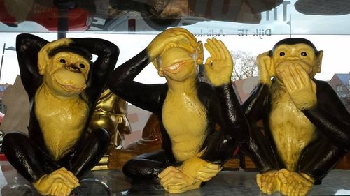 Drie geel-zwarte apenbeeldjes die poseren met hun handen op hun hoofd, oor en mond.