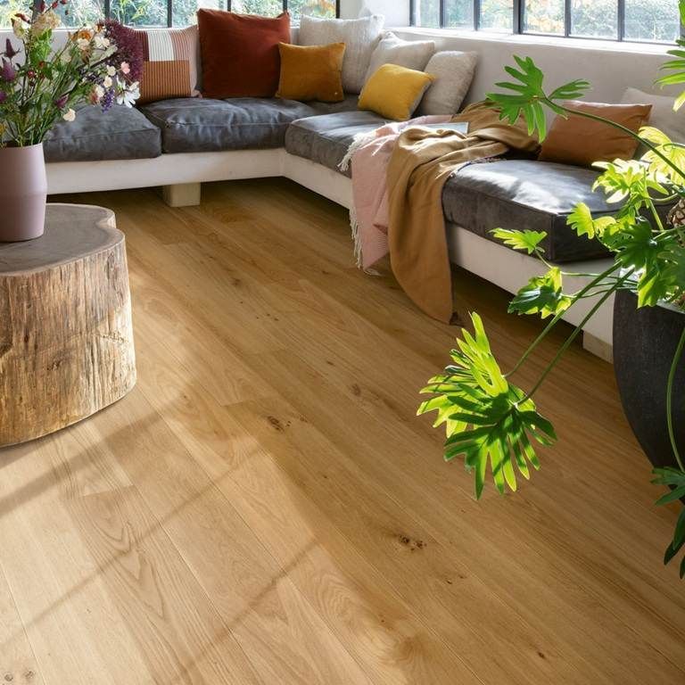 Helles Wohnzimmer mit grauer Eckcouch, farbenfrohen Kissen, Holzboden und Pflanzen an grossen Fenstern