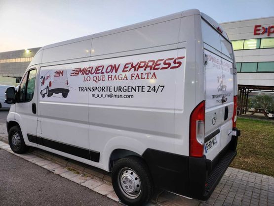 Una camioneta blanca con escritura en español en el costado está estacionada frente a un edificio.