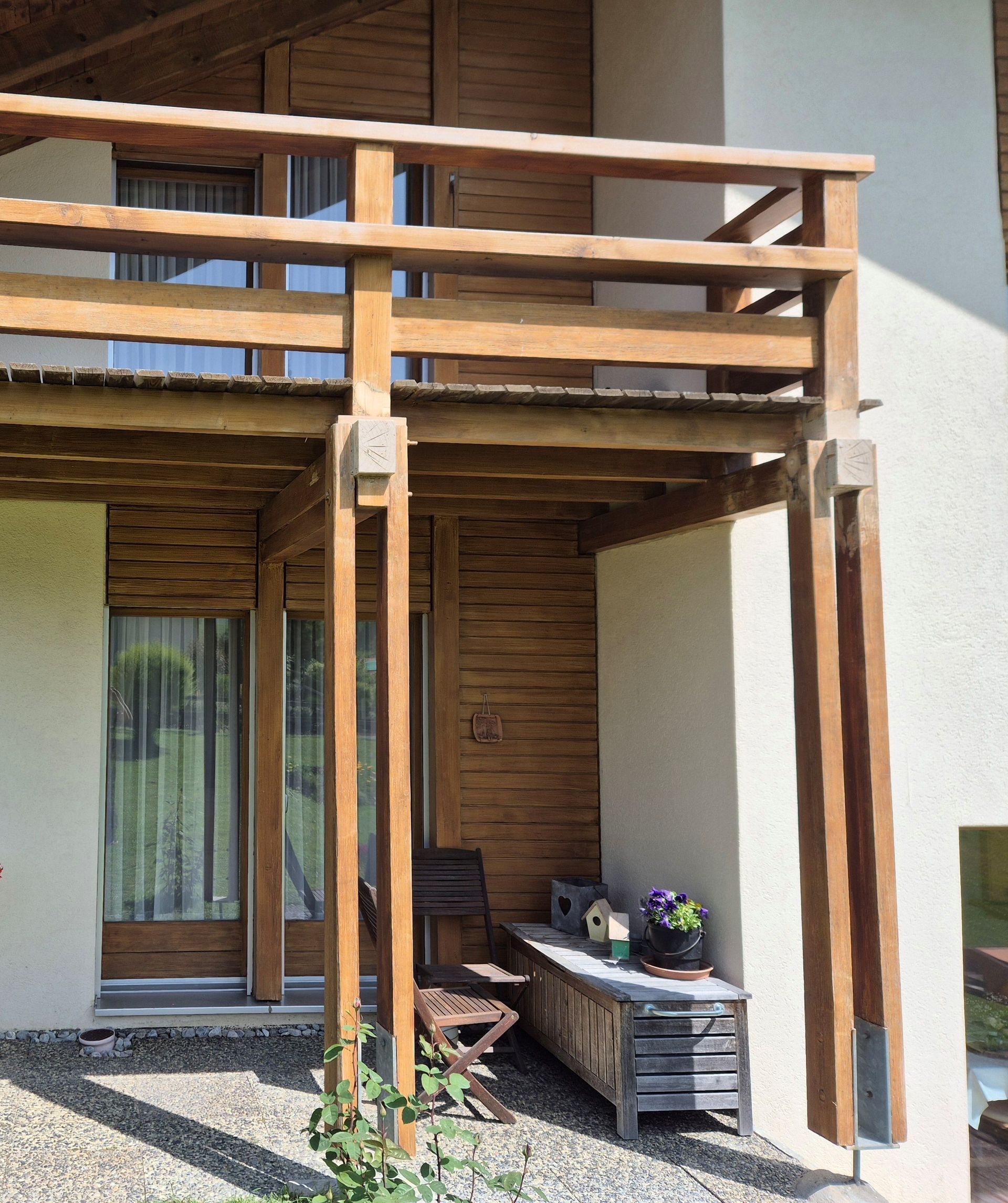 Balcon et porche en bois avec un patio en pierre, entouré d'un bâtiment beige clair.