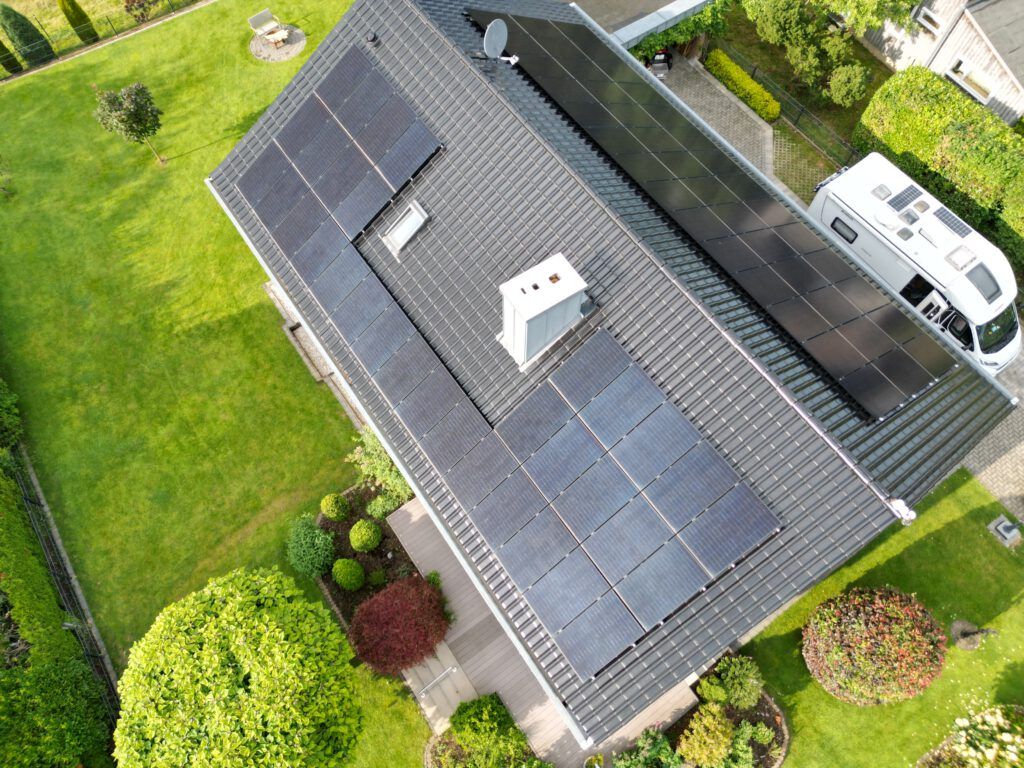 Draufsicht auf ein Haus mit Solarmodulen auf dem Dach und einem in der Einfahrt geparkten Wohnmobil.