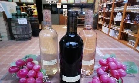 Tres botellas de vino están junto a las uvas en una tienda.