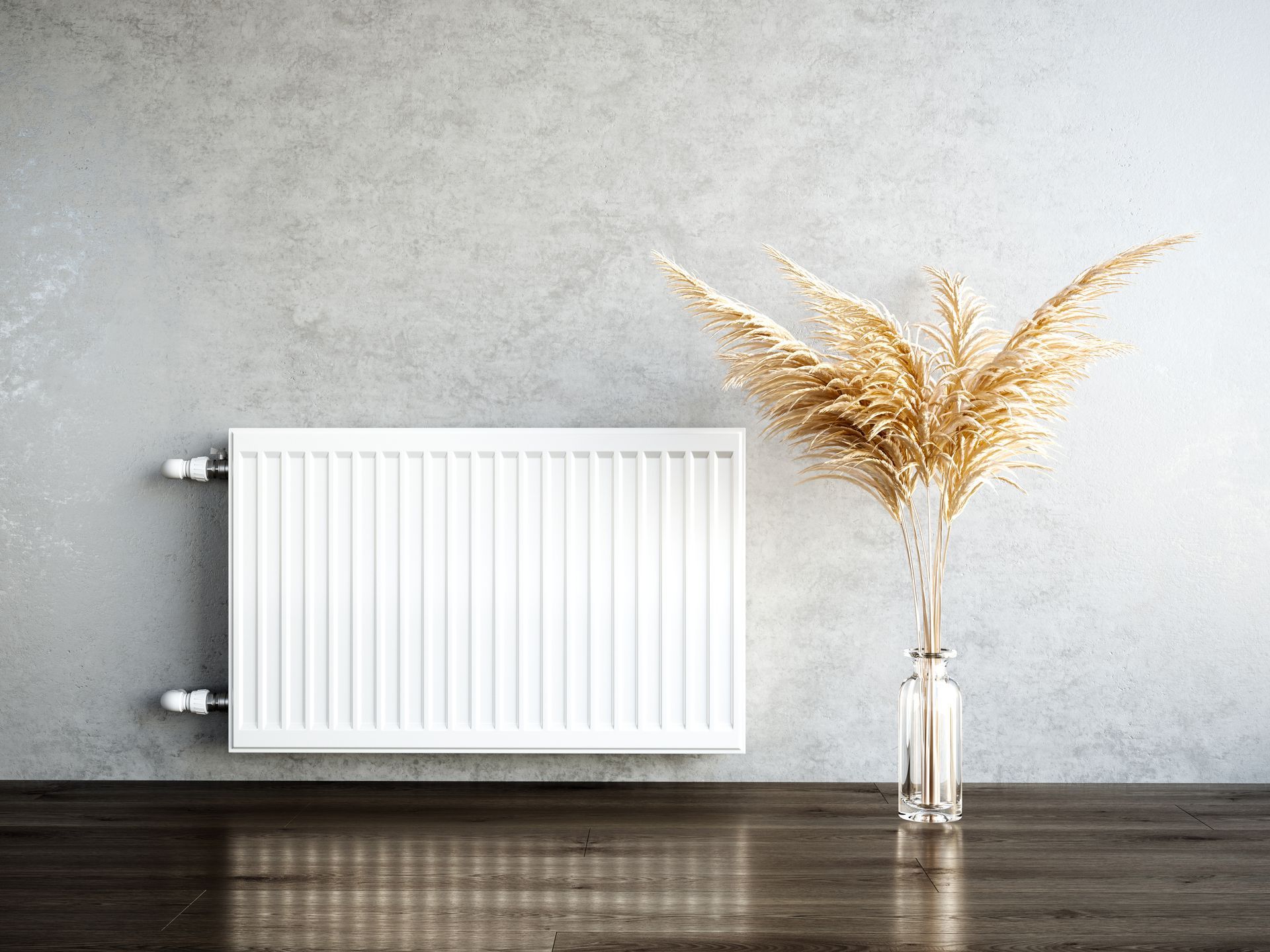 Radiateur blanc sur un mur gris, à côté d'un vase en verre contenant du blé doré séché. Sol en bois foncé.