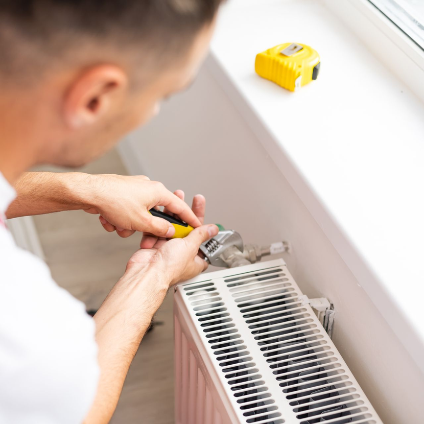 Une personne utilise une clé à molette pour réparer un radiateur près d'un rebord de fenêtre.