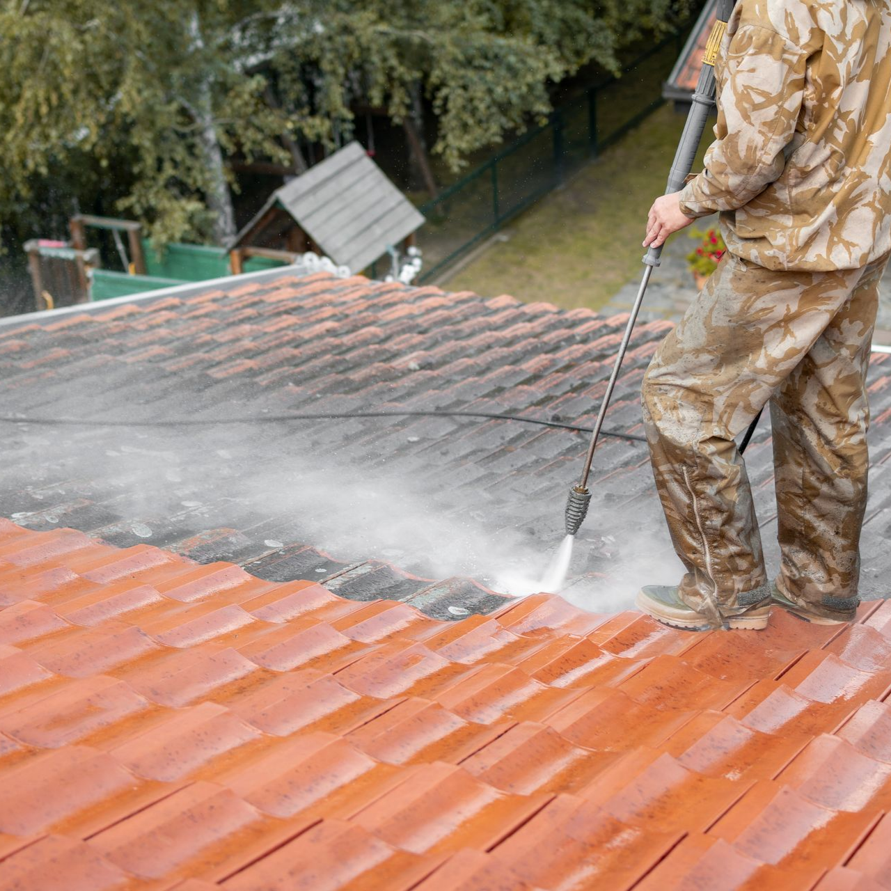 Une personne nettoie à haute pression un toit en tuiles rouges