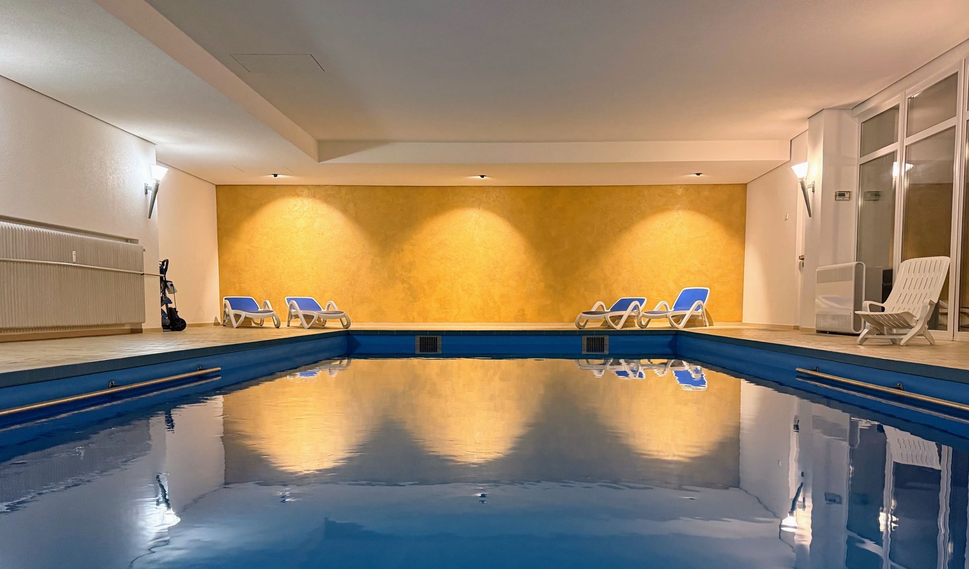 Innenpool mit Liegestühlen und warm beleuchteter Wand im Wellnessbereich der Ferienanlage in Schönwald im Schwarzwald