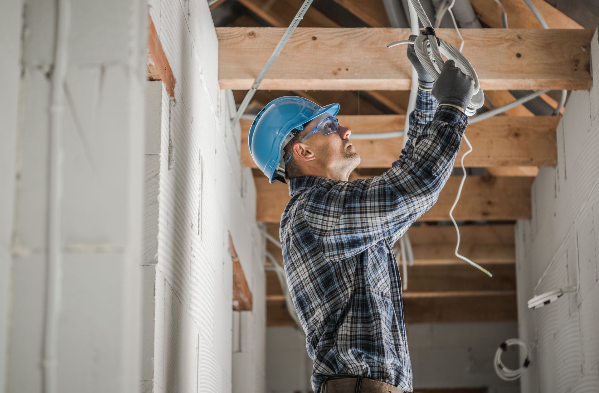 Un électricien portant un casque et des lunettes de sécurité travaille sur le câblage d'un chantier de construction.