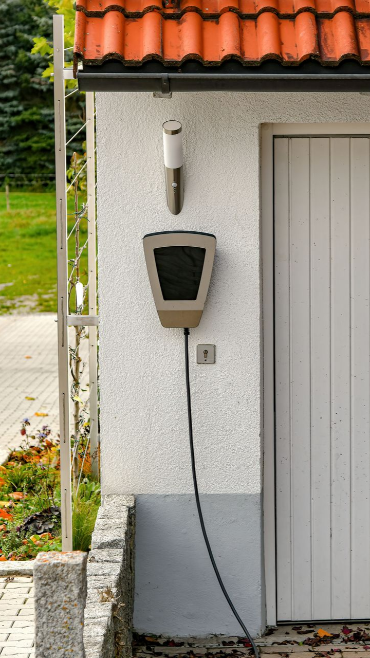 Borne de recharge pour véhicules électriques sur un mur blanc texturé, près d'une porte blanche, avec un toit rouge.