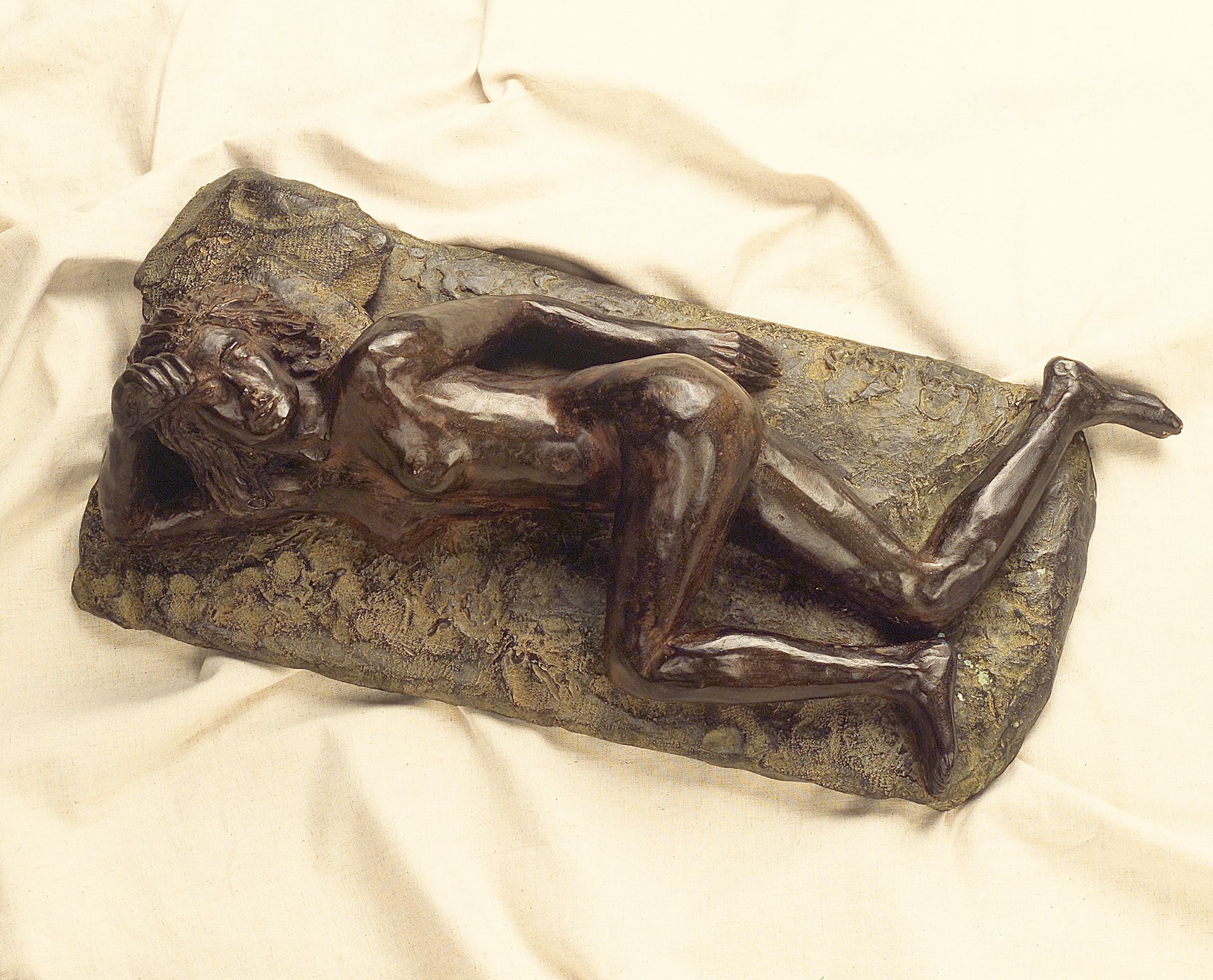 Una estatua de bronce de una mujer recostada sobre una roca.