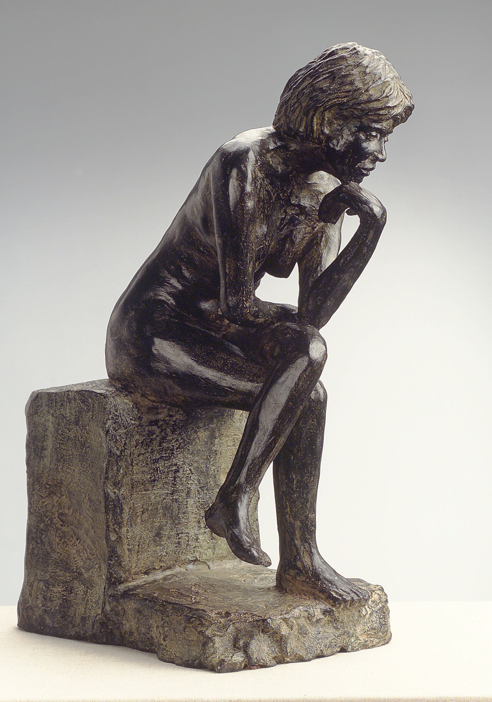 Una estatua de una mujer sentada en una roca pensando.