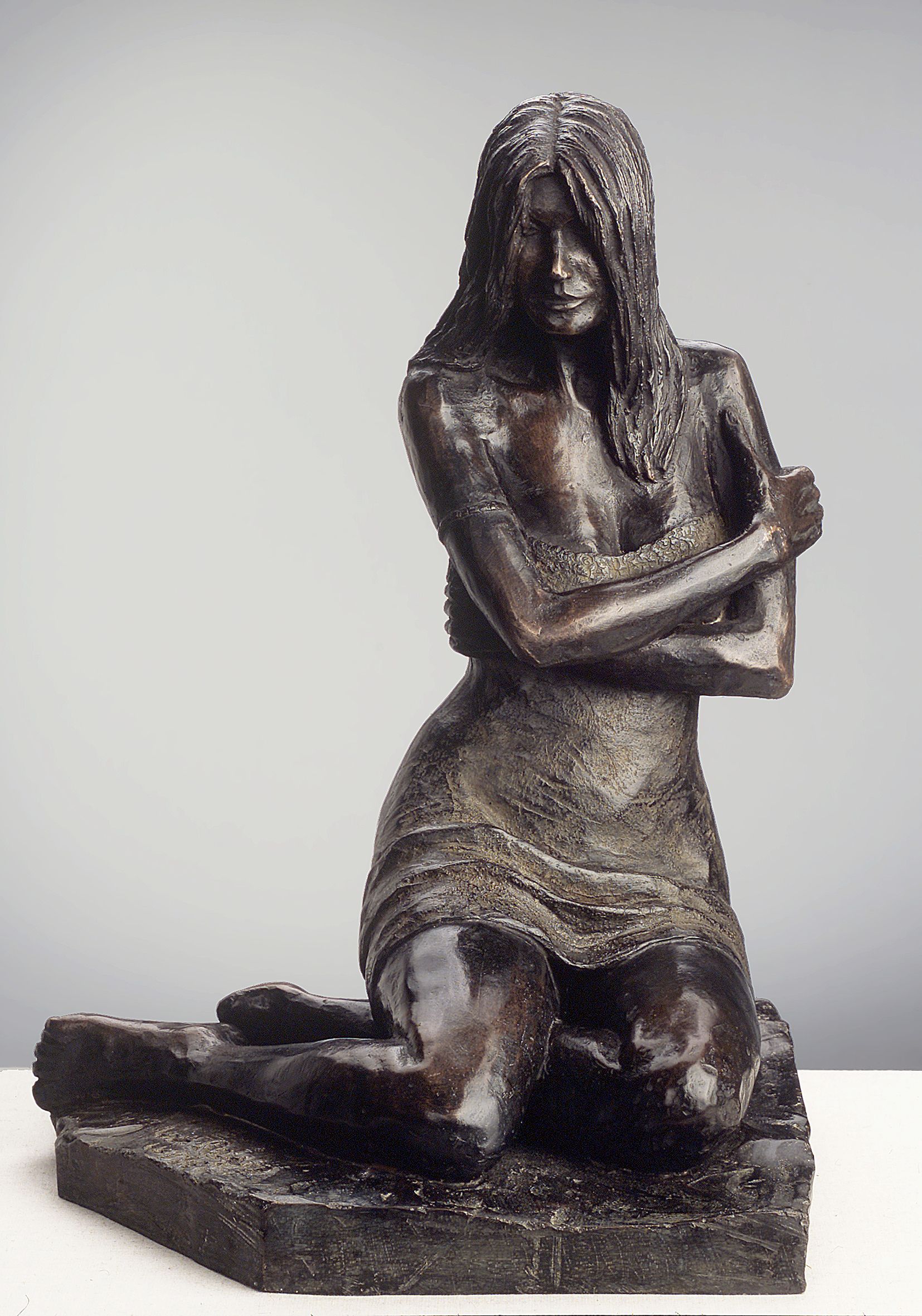 Una estatua de bronce de una mujer arrodillada con los brazos cruzados.