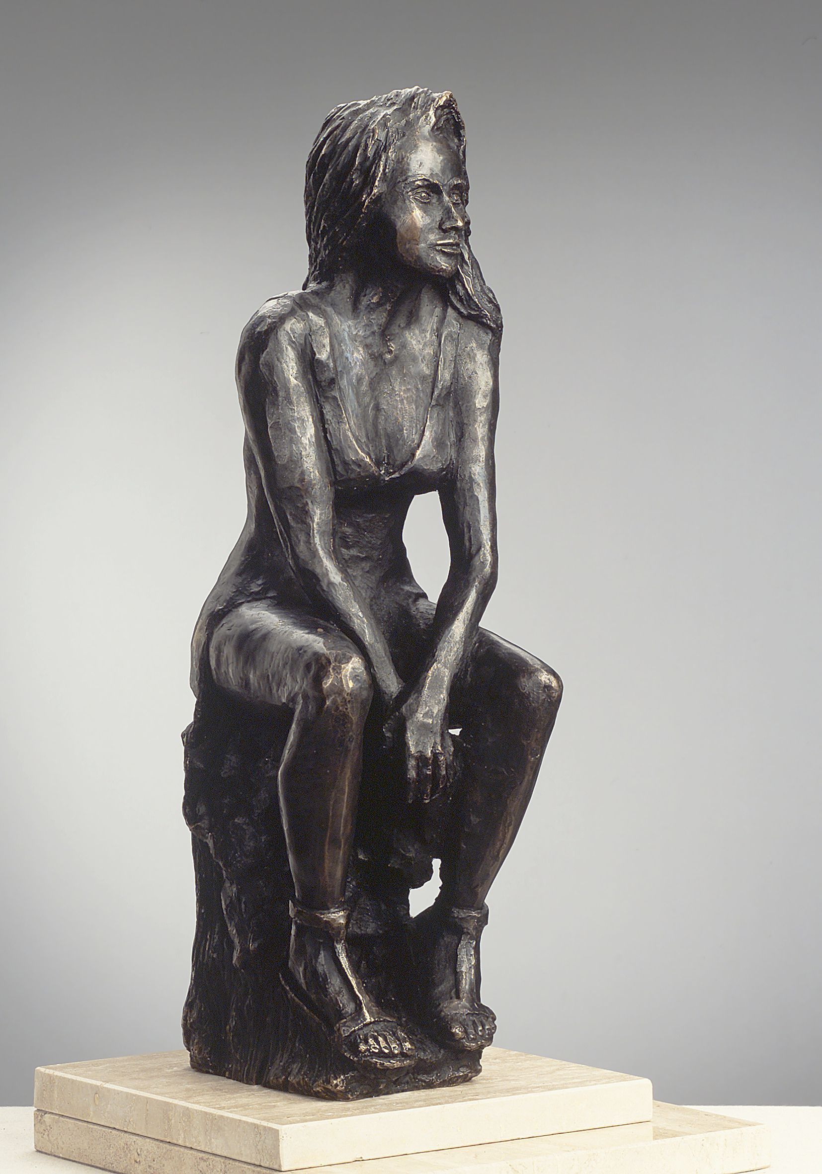 Una estatua de bronce de una mujer sentada en una roca.
