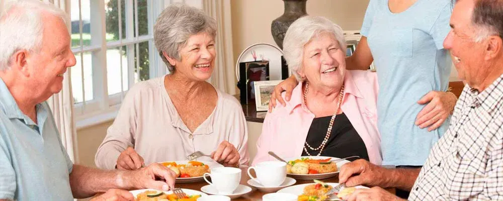 Un grupo de personas mayores están sentadas alrededor de una mesa comiendo comida.