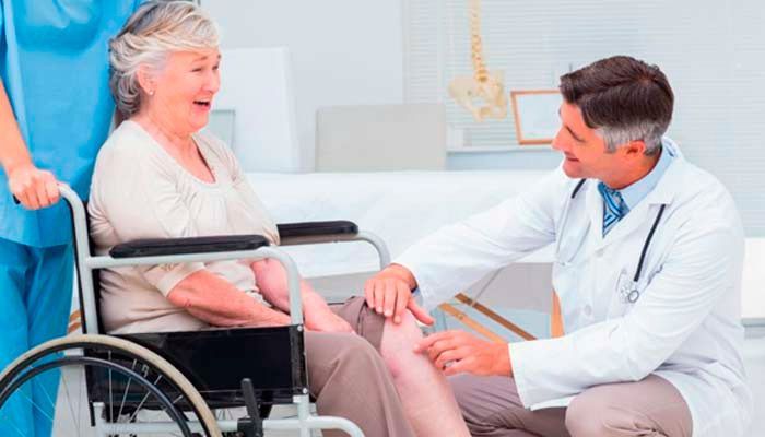 Un médico examina la rodilla de una anciana en silla de ruedas.