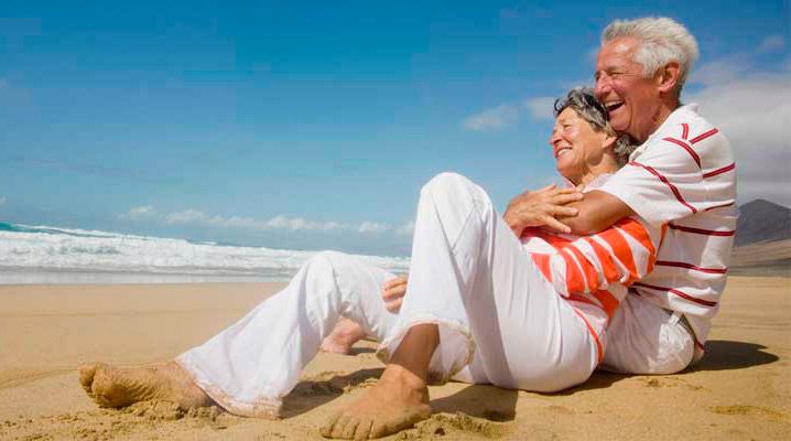 Una pareja de ancianos está sentada en la playa abrazándose.