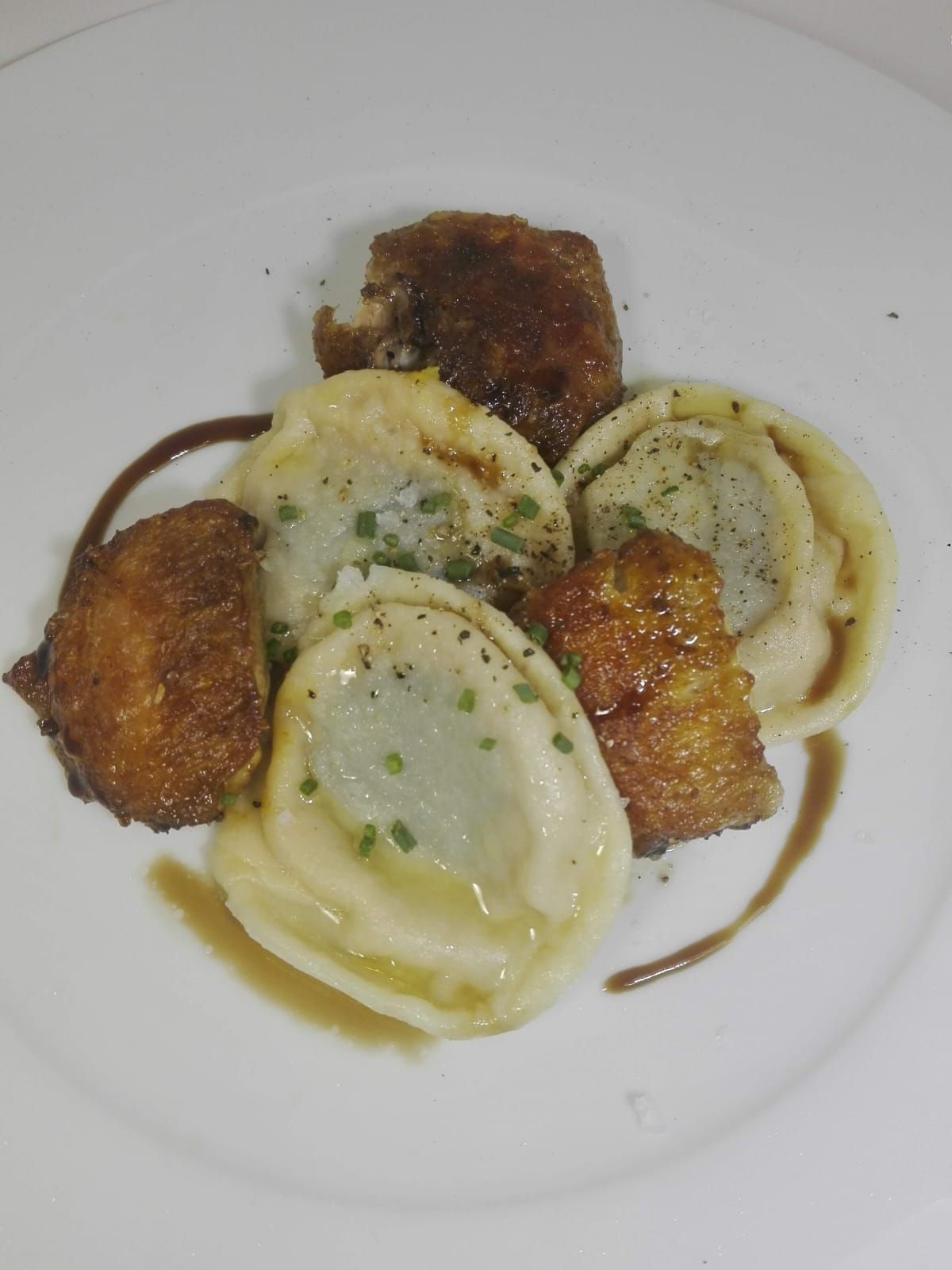 Raviolis emplatados con rodajas de champiñones dorados y guarnición de hierbas en un plato blanco.
