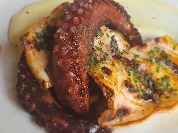 Pulpo a la parrilla y pescado sellado con hierbas en un plato blanco.
