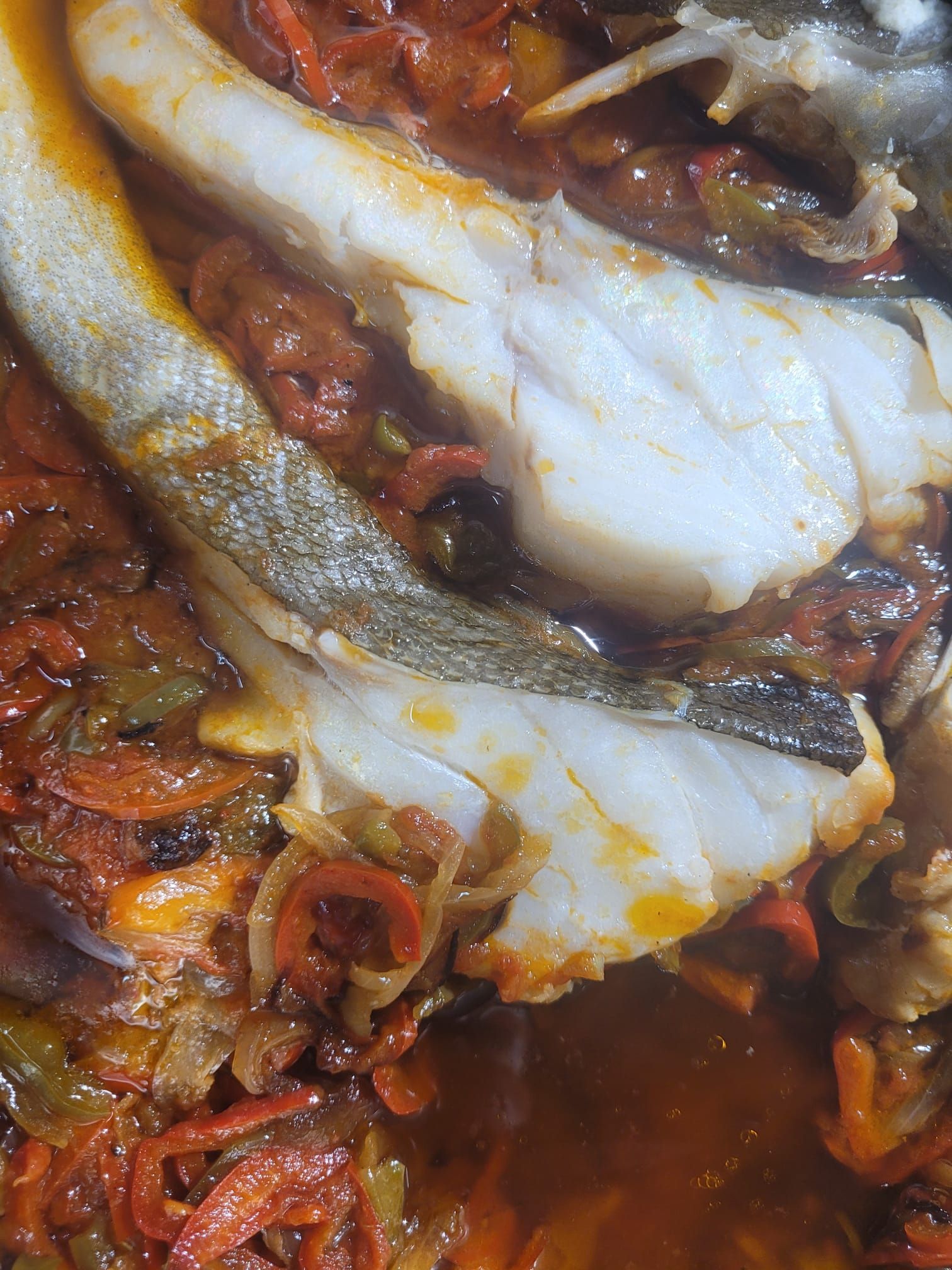 Primer plano de un pescado en salsa roja con especias y rodajas de cebolla.