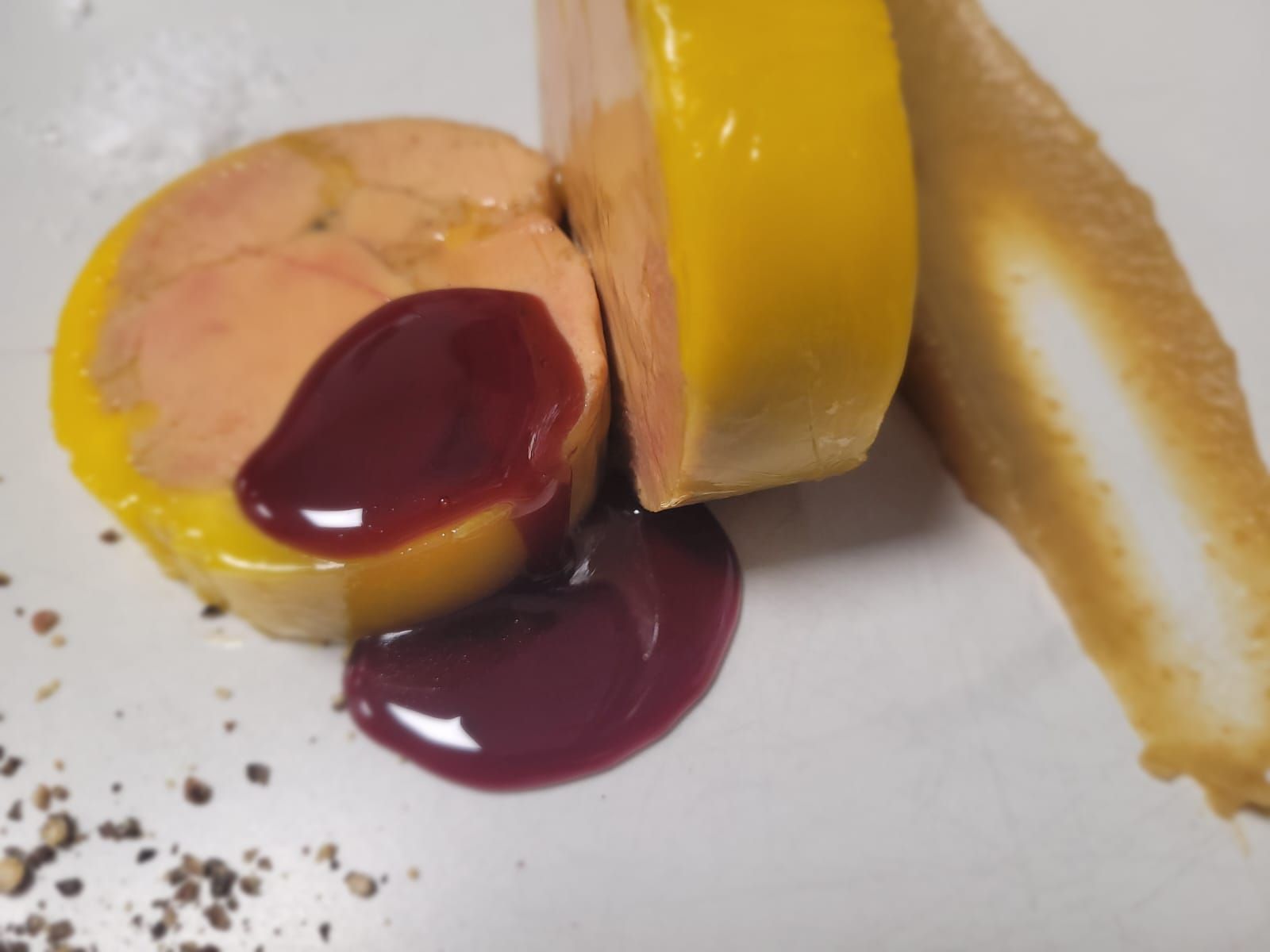 Postre amarillo en rodajas con salsa de frutos rojos y migas sobre un plato blanco.
