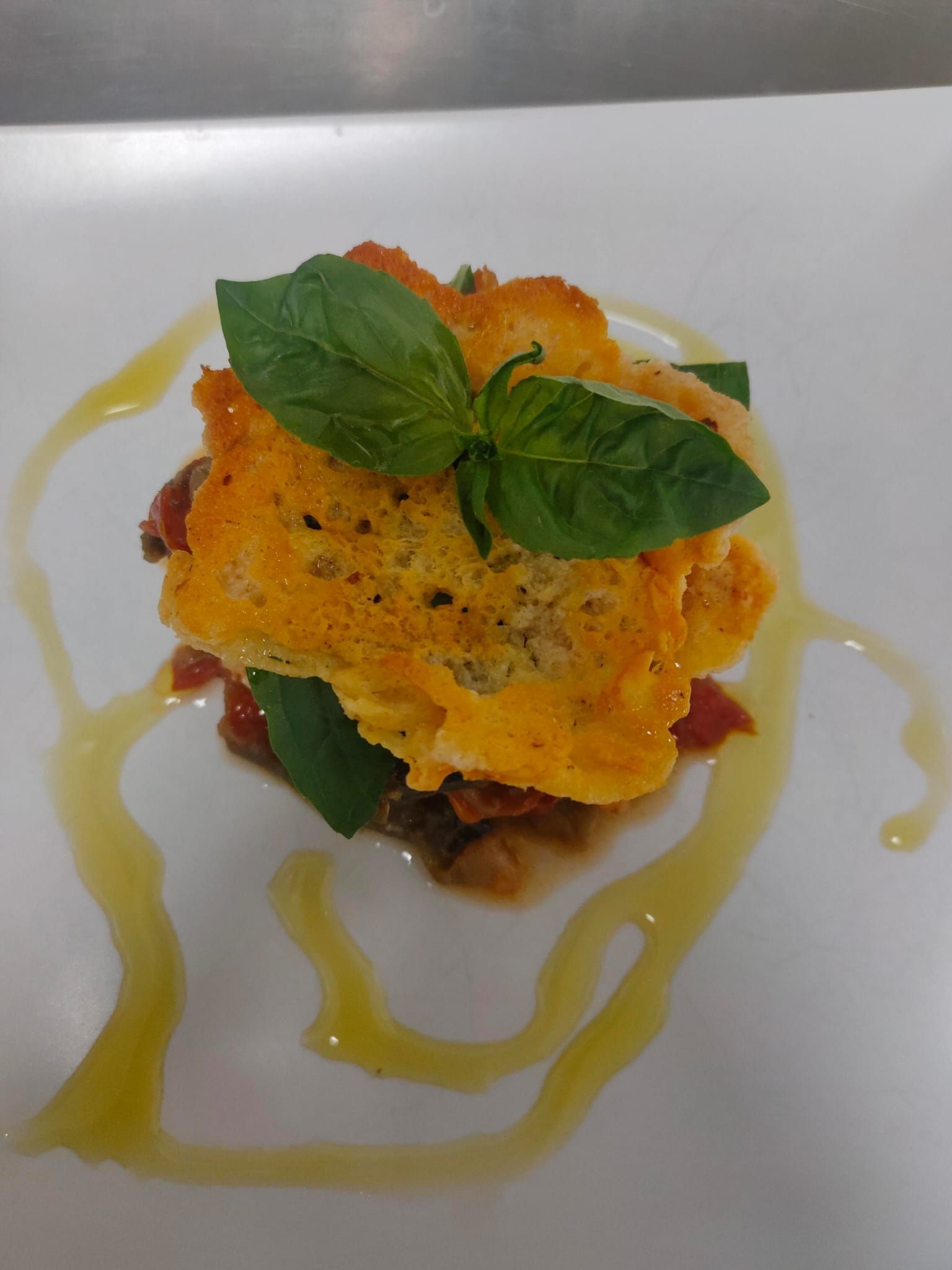 Plato gourmet emplatado con una cobertura crujiente de naranja, hojas de albahaca y un chorrito de salsa amarilla.