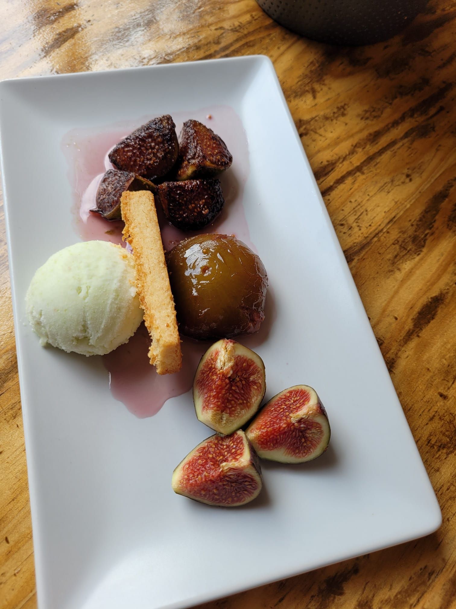 Surtido de postres en un plato blanco: helado, fresas, higos y una porción de pastel sobre una mesa de madera.