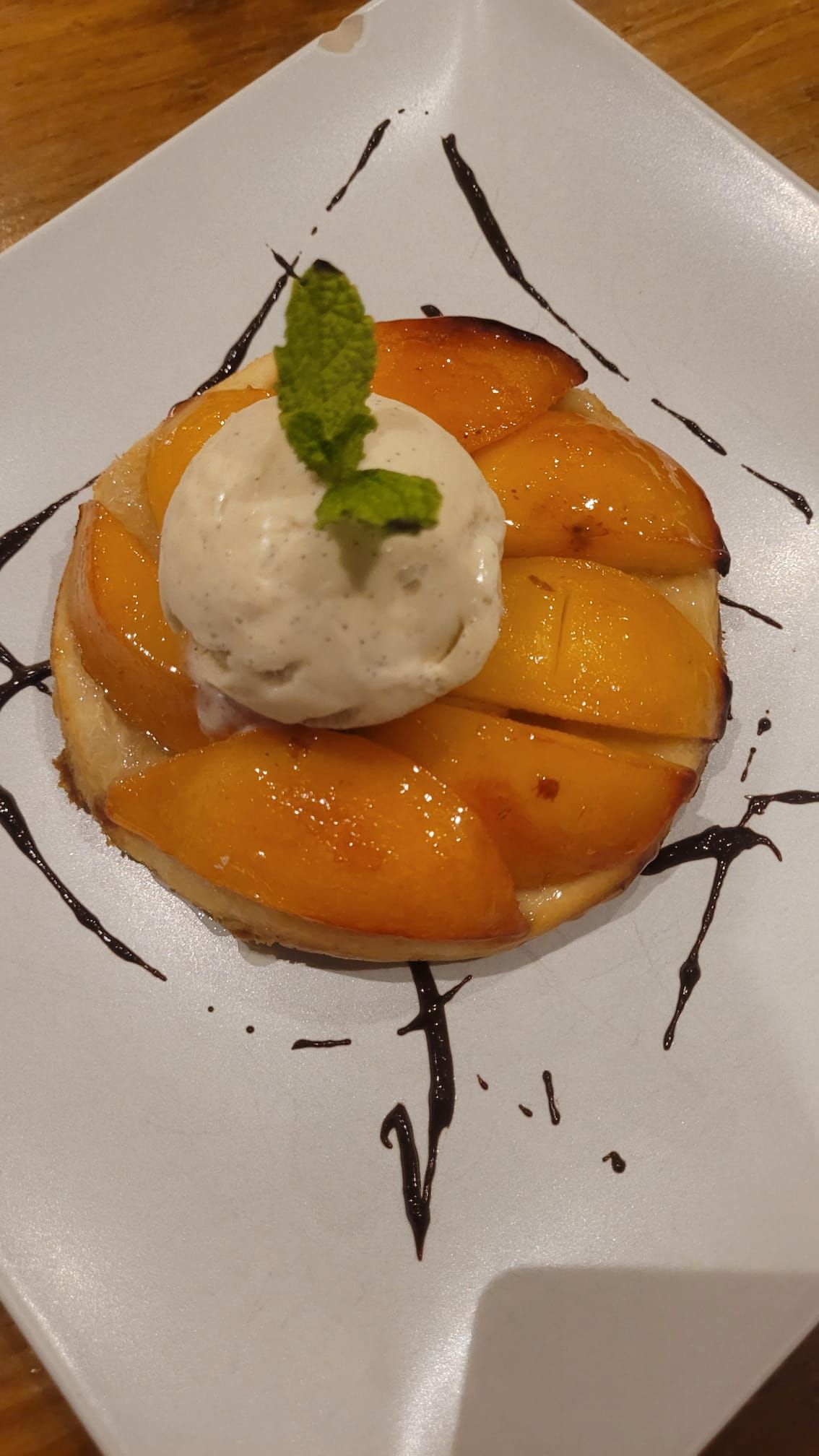 Postre con rodajas de melocotón y una bola de helado de vainilla en un plato blanco, decorado con menta.