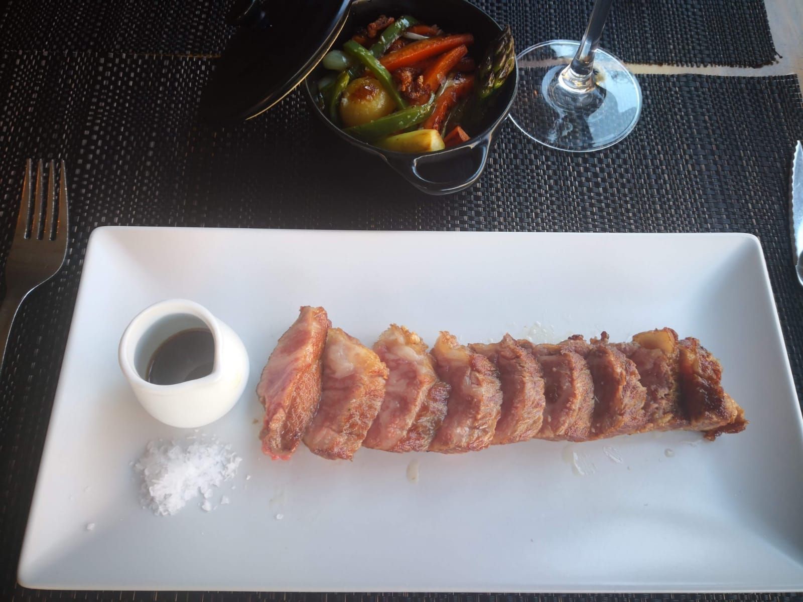 Un plato de filete sellado en rodajas, servido con un pequeño cuenco de salsa, una buena cantidad de sal y una guarnición de verduras asadas.