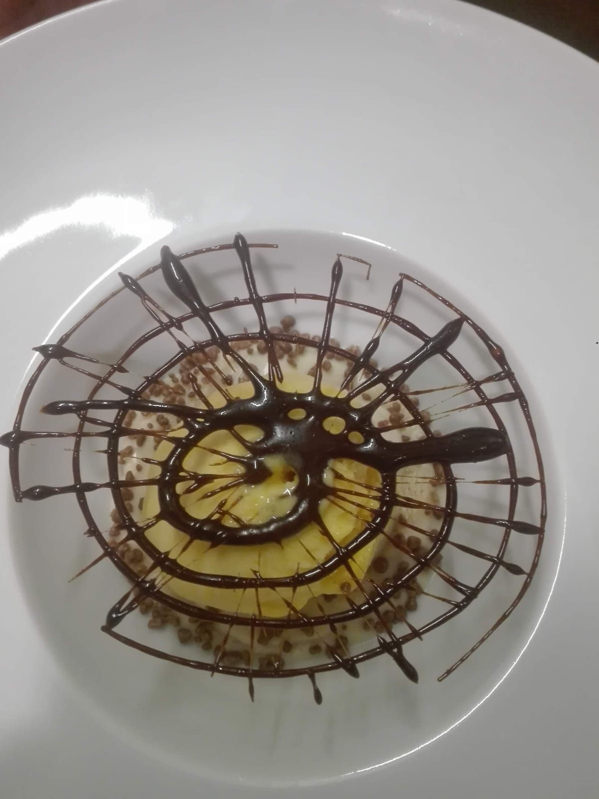 Un postre redondo decorado con un diseño de red de chocolate en espiral sobre un plato blanco liso.